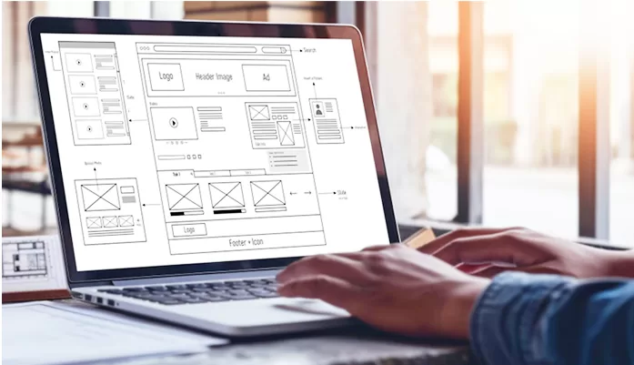 Web designer working on a laptop showing website wireframes and layout sketches